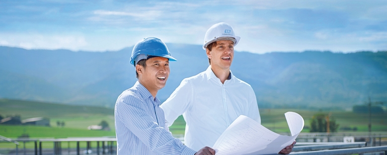 Two engineers standing on top of a storage tank in front of green landscape.