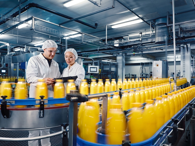 Two engineers in anbeverage plant overseeing orange juice filling process.