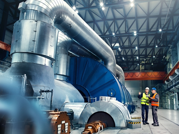 Two engineers discuss next to a power generation turbine.