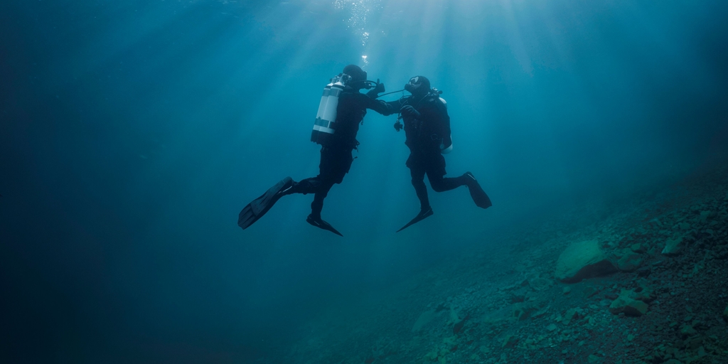 Underwater scene: a diver supports a second diver who experiences issues with the air supply.